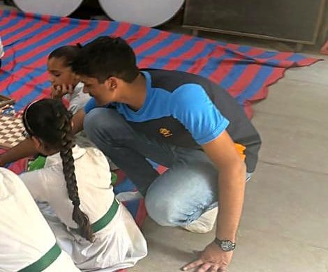 Mukund Agarwal crouches beside students at a chessboard during a school session.